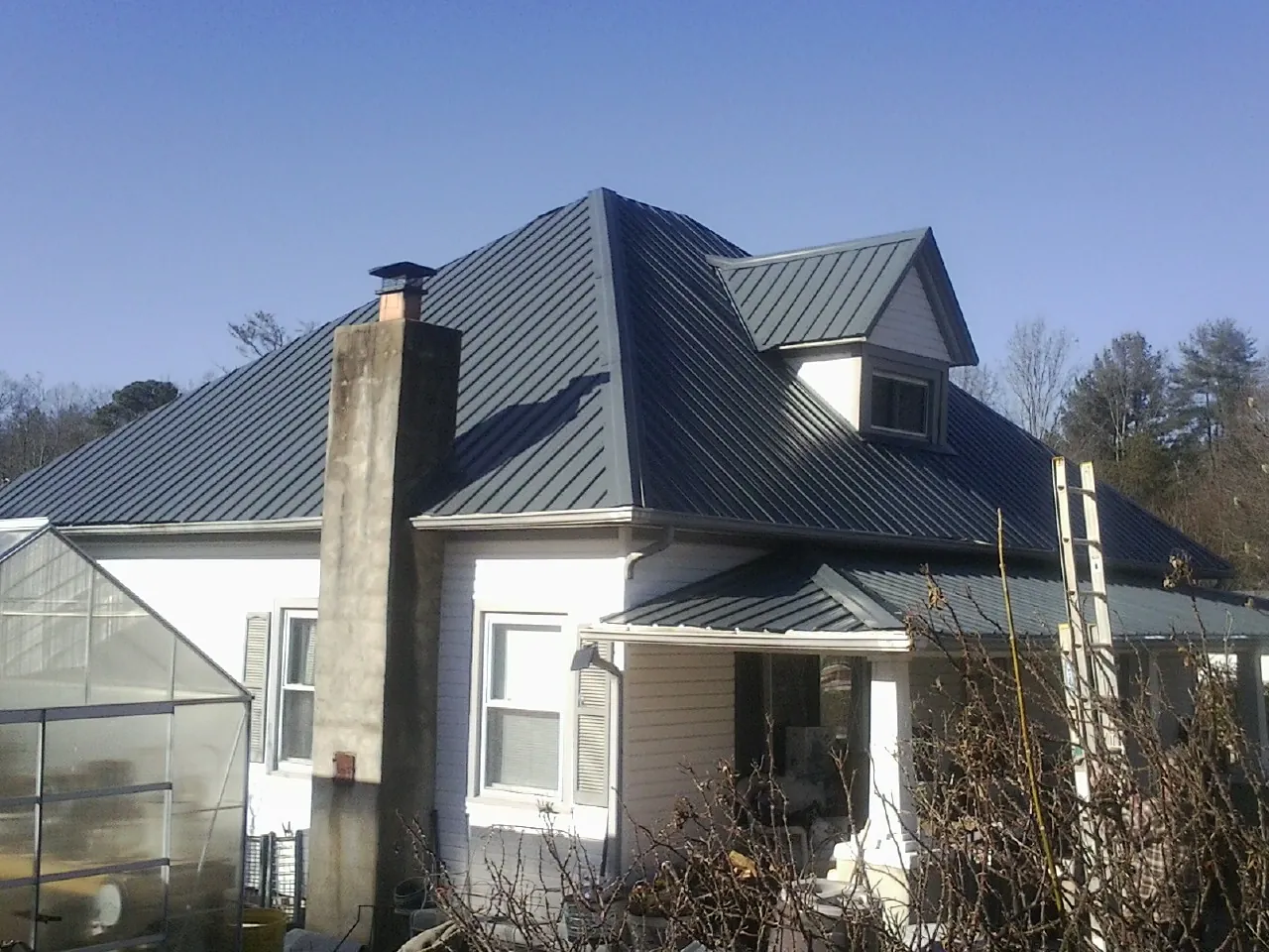 Dark blue standing seam metal roof on a white farmhouse with dormer — Slate & Tile Roof Repair by Roofing Brothers in Josephine