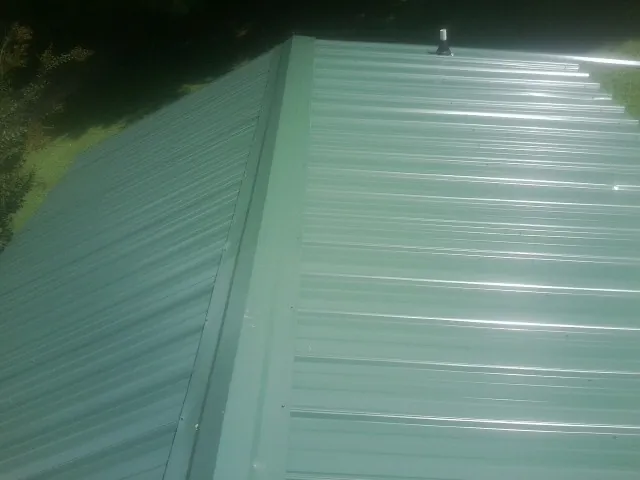 New green metal panels meeting at the ridge of a roof — Flat Roof Repair work by our crew in Josephine